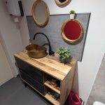 Petit WC aménagé avec un meuble en bois et noir, une vasque en cuivre et des miroirs ronds