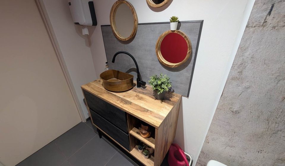 Petit WC aménagé avec un meuble en bois et noir, une vasque en cuivre et des miroirs ronds